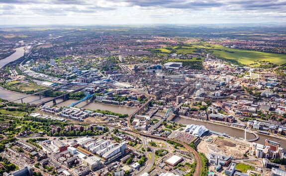 Aerial view of Newcastle upon Tyne, showing the River Tyne, city centre, bridges, and surrounding countryside.

