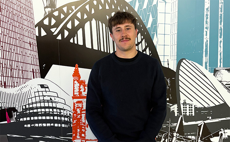 NUBS student Benjamin Collier standing in front of a mural depicting various North East landmarks	