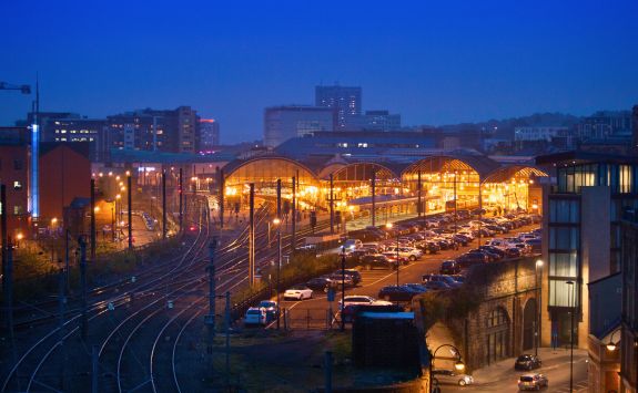 A view of Central Station in Newcastle illuminated with warm lights at night, surrounded by railway tracks and a car park.