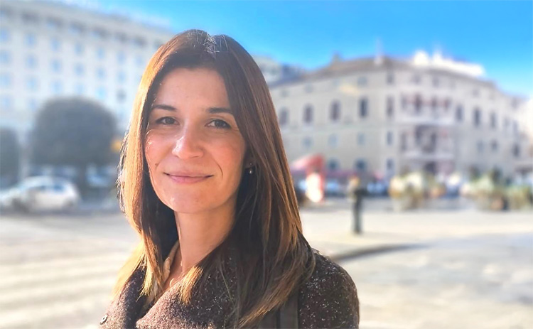 Dr Claudia Udroiu in an outdoor urban setting with historic buildings in the background.