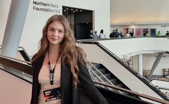 Darya Dyakun at the Thinking Digital Conference 2024, held at The Glasshouse in Newcastle. She is standing on an escalator, smiling, with the Northern Rock Foundation Hall sign visible in the background. The conference venue is modern and busy with attendees