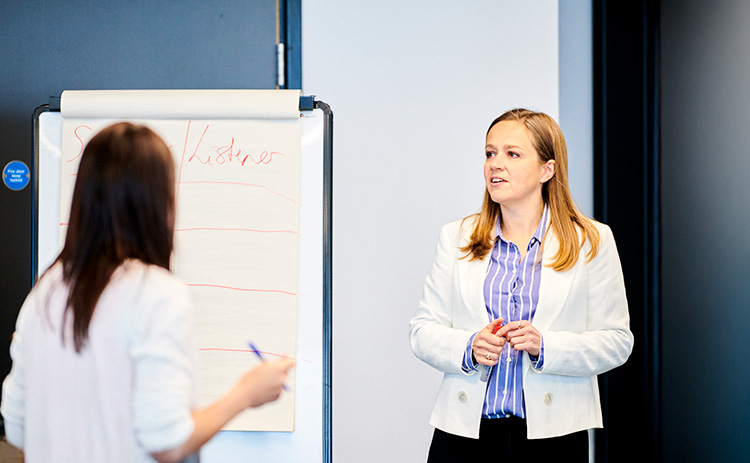 Light-skinned female executive education lecturer leading a session with a participant, using a flipchart for notes.