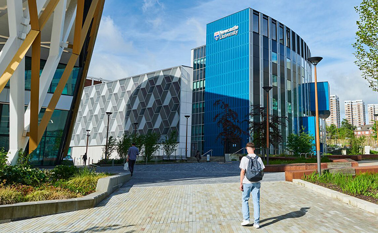 A student walks towards the Frederick Douglass Centre, a modern blue glass building at Newcastle University