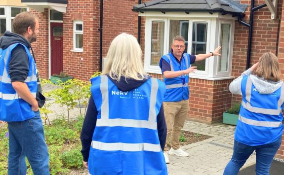 A researcher explaining features of an eco-friendly home to a group wearing blue NeTV vests at Futures Close	