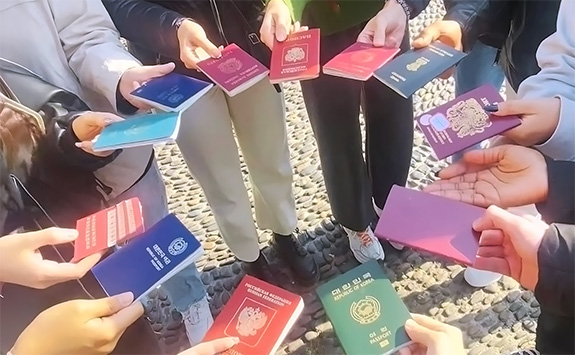 A group of students standing in a circle, each holding out a passport in front of them to form a ring.