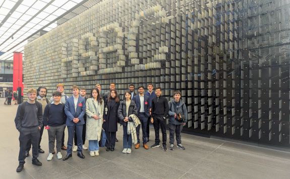 Students visiting HSBC headquarters during the student trek. The group is standing in front of a large wall displaying the HSBC logo made from digital panels.