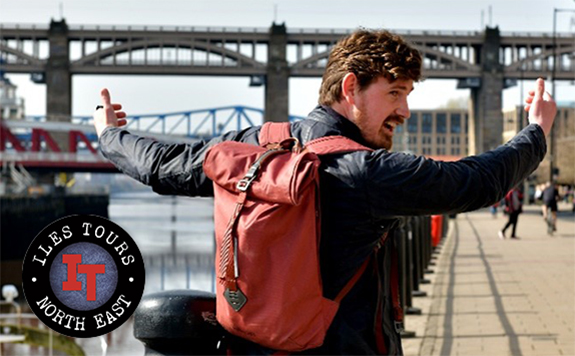 Alexander Iles wearing a dark jacket and a red backpack stands on Newcastle Quayside, gesturing towards the River Tyne and its bridges. The Iles Tours logo is in the bottom-left corner. The iconic High Level and Swing Bridges are visible in the background.