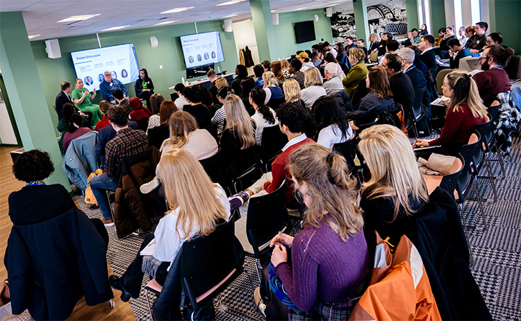 A crowd of people sat in the St James View room, as a panel of four experts have a discussion at the front of the room	