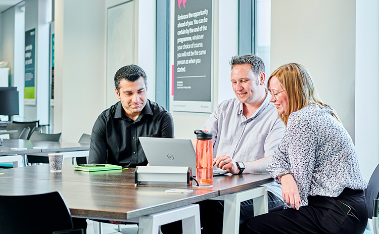 Three Newcastle University MBA students sat around a laptop at a table in a seminar room