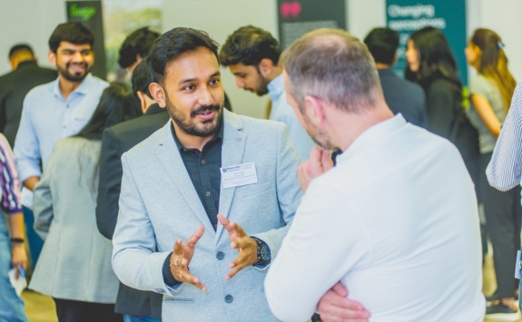 Newcastle University Business School students and alumni networking at a professional event in the Business School, with one student engaging in conversation and others mingling in the background.