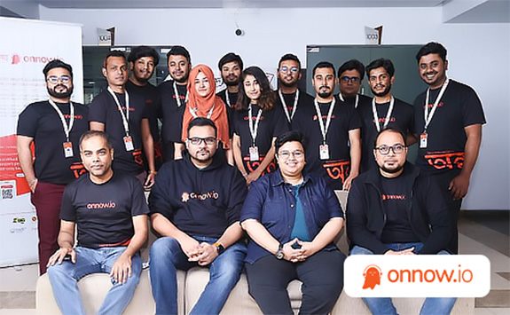 A group of 16 team members from Onnow.io pose for a photo in an office setting. They are wearing branded black T-shirts with the company logo, and some have ID badges. A banner with the Onnow.io branding is visible in the background. The Onnow.io logo is displayed in the bottom right corner.