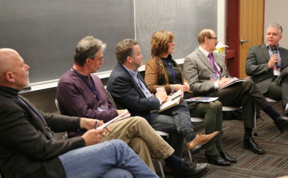 From left to right: Roy Suddaby, Peter Elson, James Stauch, Sandra Hucaluk, Charles Harvey, and Robin McLay seated during a panel discussion in front of a blackboard. Robin McLay is speaking into a microphone while the others take notes.