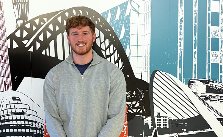 NUBS student Ross Mackenzie standing in front of a mural depicting various North East landmarks	