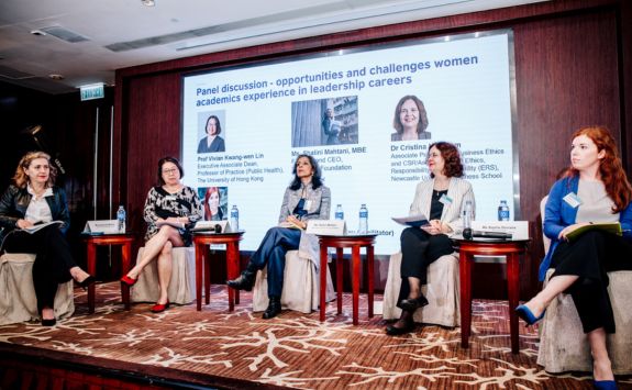 A panel discussion titled "Opportunities and Challenges Women Academics Experience in Leadership Careers." The panel features five women, including Dr Cristina Neesham. Background includes a screen with information about the panel and its participants.
