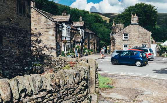 A quaint village street in Edale, Peak District. Stone houses and shops line the street. In the background, green hills rise up.