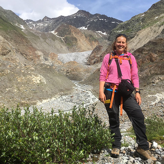 Professor Bethan Davies standing on a rocky mountainside, with a snowy mountain in the background. 