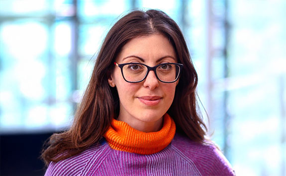 Lenia is wearing glasses with a purple and orange sweater. 